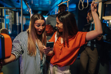 Excited young women sharing exciting news on smartphone on bus