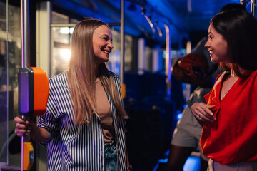 Two smiling women talking on a moving bus at night