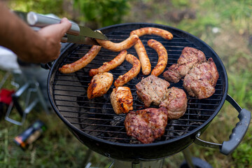 Grilling meat and sausages on charcoal barbecue. Close-up of assorted meats and sausages cooking on...