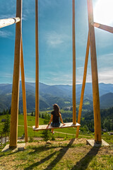 Woman on giant swing overlooking mountain valley. A young woman relaxes on a large wooden swing,...