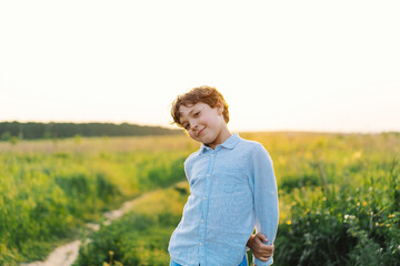 A joyful child stands in a vibrant green field during sunset, smiling and playfully posing with a...
