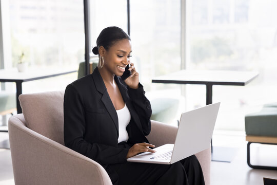 Successful phone negotiations. Smiling confident Black businesswoman working on distance discuss deal with customer by telephone offer advice support to client using electronic documents on notebook