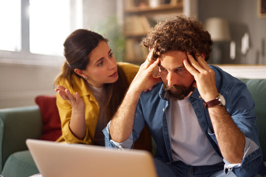 A woman gestures while expressing concern, and a man appears stressed, holding his head in distress as they address their financial issues at home. - Powered by Adobe