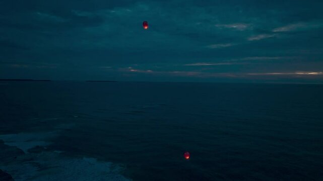 Paper lanterns lit at dusk over the sea. Paper lanterns flying in the sky