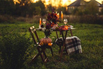 Elegant autumn decoration. Private wedding party for two, table set with floral decor, pumpkins, wine in field or meadow. Fall vibes, sunset, golden hour. Romantic surprise, marriage proposal