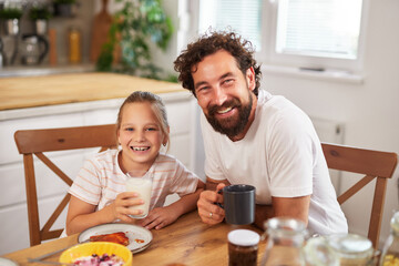 A father and daughter enjoy breakfast together in a warm kitchen, sharing joyful moments, laughter, and food on a bright morning.