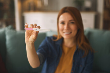 A woman with long red hair smiles widely as she holds a positive pregnancy test, surrounded by a...