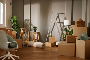 A cozy room filled with unpacked boxes, stools, and a ladder while plants add a touch of green....