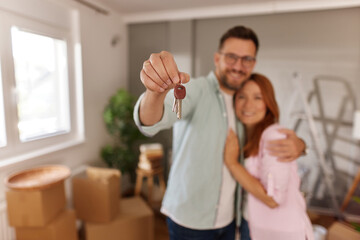 A couple joyfully celebrating their new home while holding house keys. They embrace in front of...