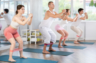 Obraz premium Group of four young people engaged in half-squatting with rubber band in fitness hall