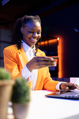 Smiling woman excited to do online shopping, typing debit card information on laptop in apartment....