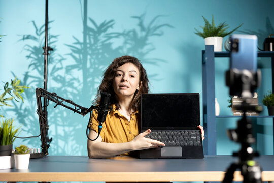 Tech expert filming review of newly launched gaming laptop, unboxing it and giving feedback to fanbase. Internet star endorsing sponsor branded notebook to subscribers, recording with phone