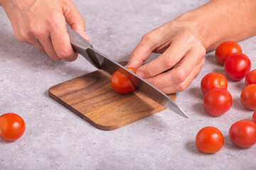 The housewife slicing fresh tomatoes with a large kitchen knife on a wooden chopping board, closeup with selective focus