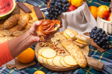 Close-up view of a picnic with food laid out and hands holding food, selective focus. The concept of summer outdoor recreation on the weekend