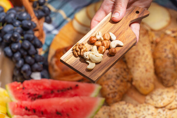 Close-up view of hand with nuts against the background of laid out picnic food, selective focus. The concept of summer outdoor recreation on the weekend