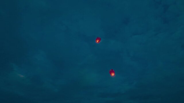 Paper lanterns lit at dusk over the sea. Paper lanterns flying in the sky