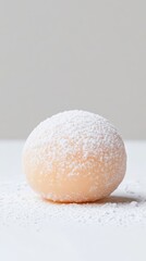 A single round dessert ball dusted with powdered sugar on a white surface against a neutral background.
