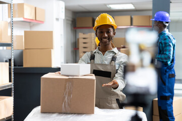 Employee recording a live tutorial in an industrial warehouse, showcasing product handling,...