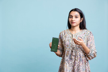 Confident woman presenting green screen on mobile gadget, standing against studio background....