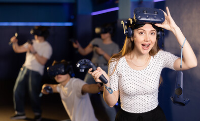 Cheerful emotional young woman in VR headset on head with joysticks in hands looking with excited...