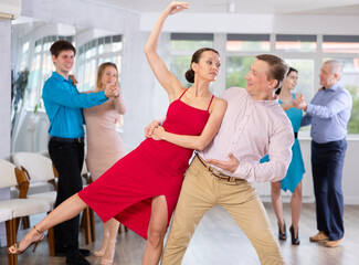 Positive young adult woman learning to dance Viennese waltz with male partner in choreography class, performing elegant support..