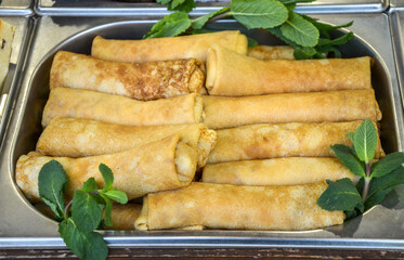 Tray of appetizing golden pancake rolls accompanied by fresh mint leaves served ready to eat