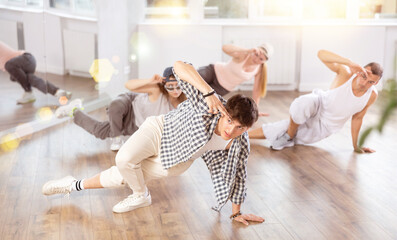 Concetrated young guys and girls studying movement of contemporary dance in classroom with his friends