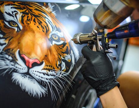 Artist airbrushing vibrant tiger on car: detailed automotive art in progress