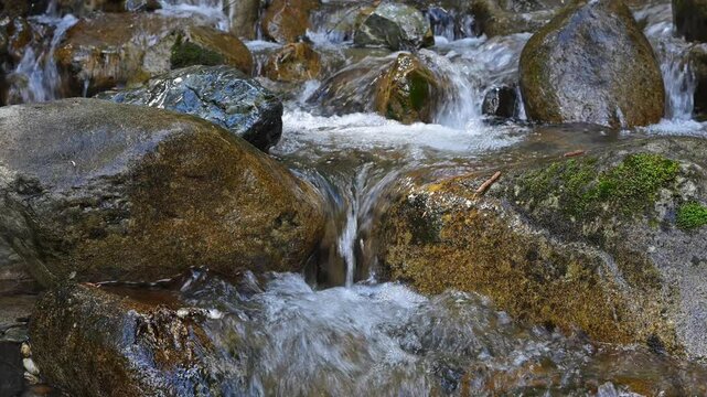 Stream falling over smooth dark rocks with tiny waterfall between large boulders in closeup as a babbling brook
