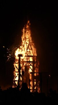 Slow motion 4x video of a wooden bonfire structure from Alicante burning at night, with flames dancing slowly through the frame during the traditional San Juan celebration.