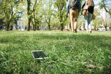 Cell phones are left on the grass as young people walk away leaving them.