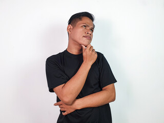 A young Asian man stands thoughtfully with his hand on his chin, wearing a black shirt against a...