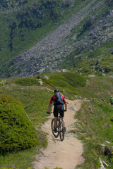 Fototapeta premium Experience mountain biking adventure! A cyclist conquers a rugged mountain trail under a bright sky, embodying the thrill of outdoor sports and exploration in a stunning alpine landscape.