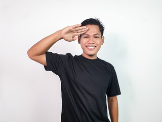 A cheerful Asian young man in a plain black shirt saluting confidently. The image reflects...