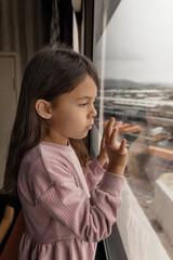 Little child girl standing near the window in hotel room, childhood memory concept