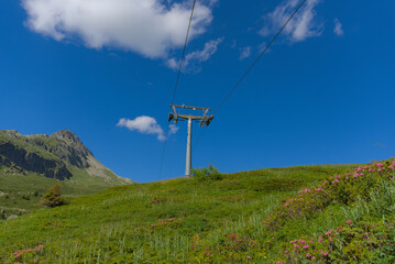 A vibrant summer mountain landscape features a ski lift ascending a lush green slope under a clear...