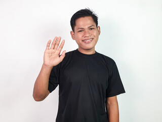 Young Asian Man in Black Shirt Smiling Waving Hand in Friendly Gesture on Plain White Background.