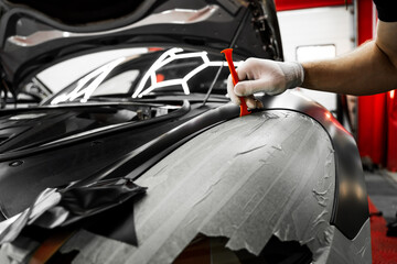 Trim tool to apply matte black wrap around a car panel edge. Car Wrapping with Trim Tool. Car detailing applies vinyl wrap around trim using plastic wedge tool for seamless finish.