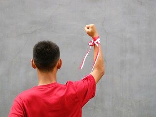 Young boy in red shirt with Indonesian flag on his shoulder, his fist raised upwards, during...