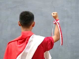 Young boy in red shirt with Indonesian flag on his shoulder, his fist raised upwards, during...