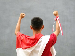Young boy in red shirt with Indonesian flag on his shoulder, his fist raised upwards, during...