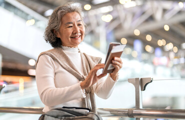 Senior asian woman holding passport and smartphone at airport showing digital travel, trip preparation and modern lifestyle for older travelers, travel app flight check-in, ticket booking, retirement
