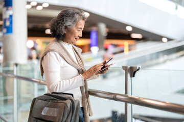 Senior asian woman holding passport and smartphone at airport showing digital travel, trip...