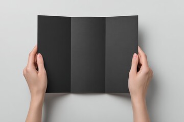 Blank black tri-fold brochure held by hands