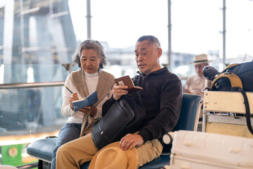 Senior asian couple sitting with luggage checking passport planning trip showing travel preparation...