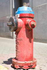 Bright red painted fire hydrant with blue cap on an urban sidewalk on a sunny day.
