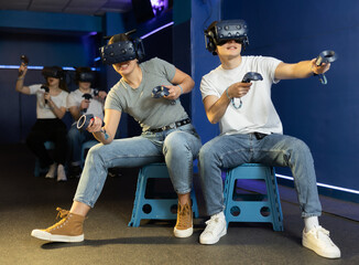 In interactive entertainment club, guy with girl in VR helmets and with joysticks sit and control...
