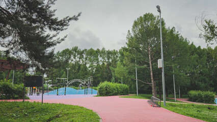 Modern outdoor playground with colorful rubber surface and climbing structures surrounded by trees, concept of childhood, recreation and urban nature