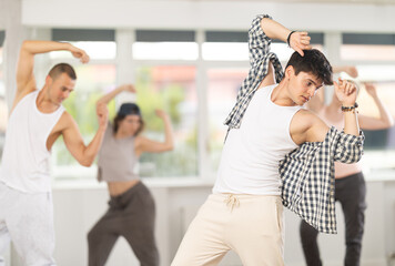 Dynamic young man training simple hip hop poses in dancehall during workout session