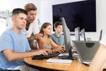 Motivated young trainee developer working at IT startup sitting at computer while male mentor explaining assigned task and giving advices on solution